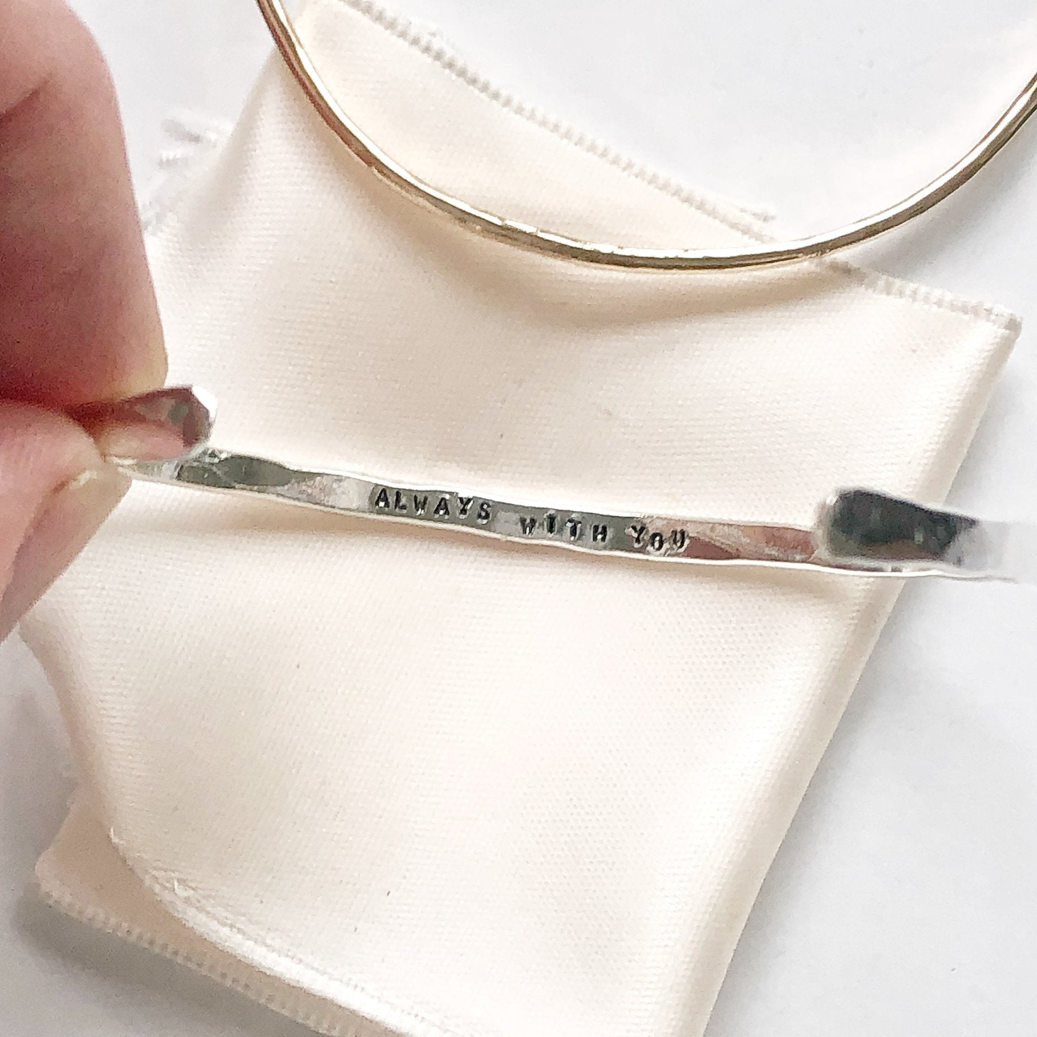2 gold and silver textured bangle bracelets with the words "always with you" stamped on the inside. Fingers holding one bracelet. Always with You Bangle by Sarah Cornwell Jewelry