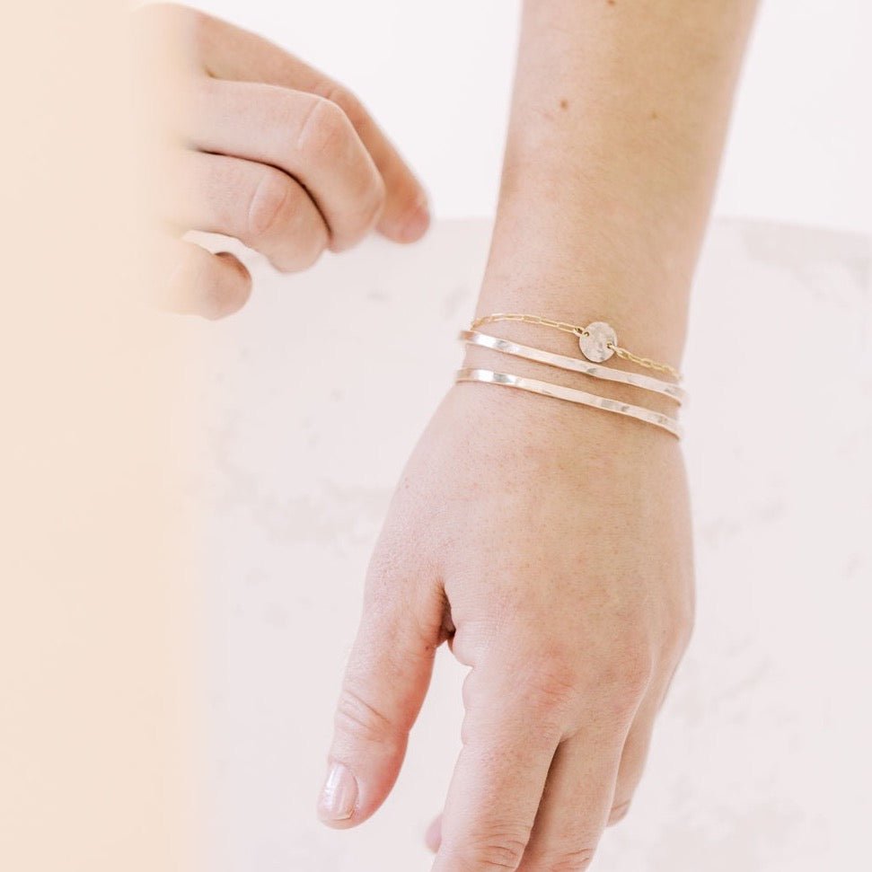 Close up of woman's wrist wearing gold textured bangle bracelets and gold textured disc bracelet. Caroline Bangle by Sarah Cornwell Jewelry