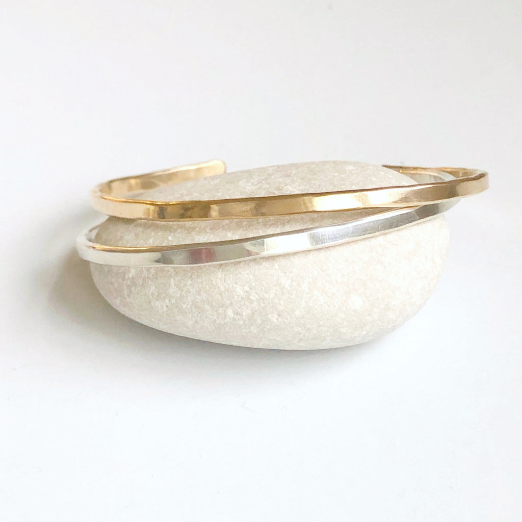 2 gold and silver textured bangle bracelets on a light gray rock. Caroline Bangle by Sarah Cornwell Jewelry
