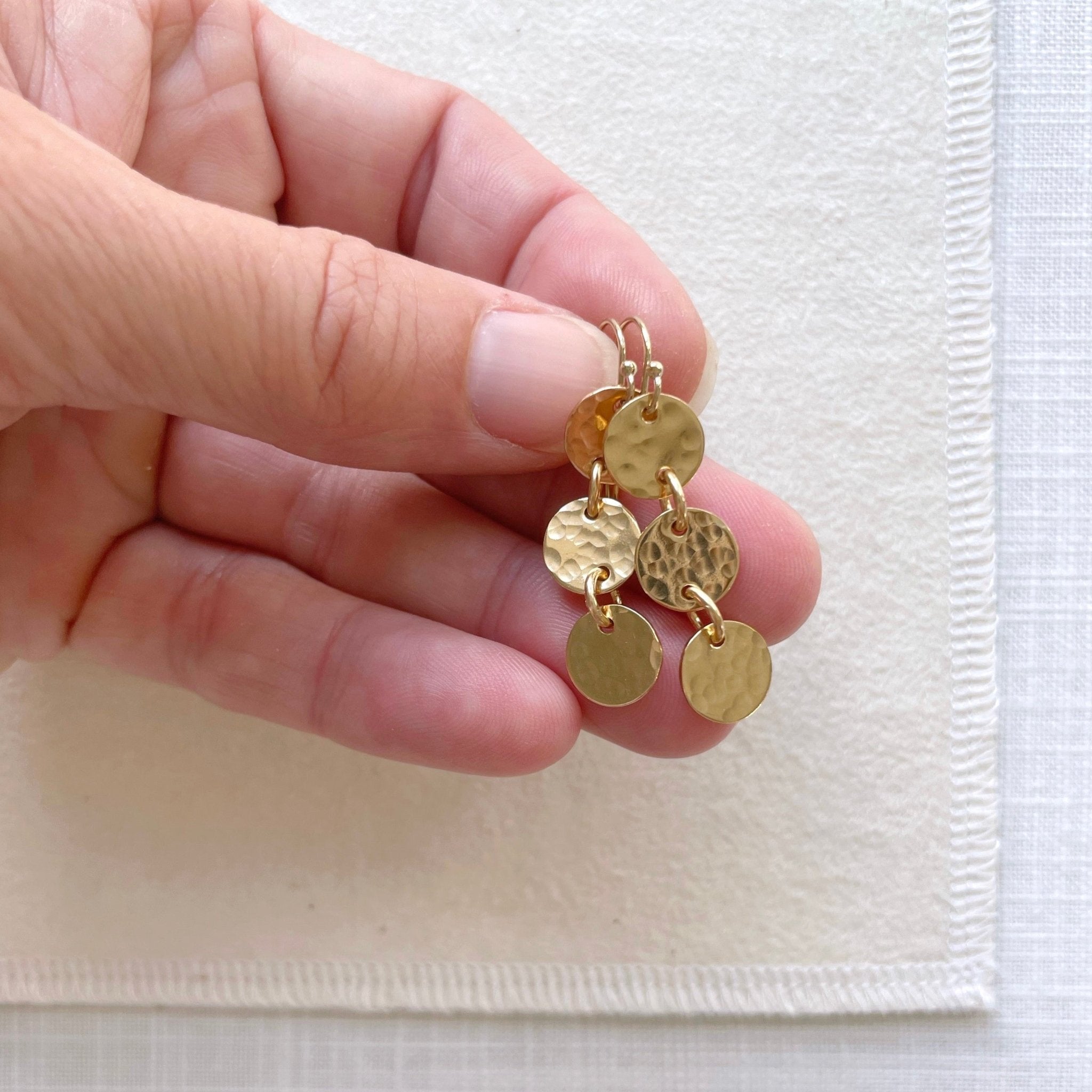 Hand holding gold 1.5 inch drop earrings with 3 same sized textured discs. Cole Earrings by Sarah Cornwell Jewelry