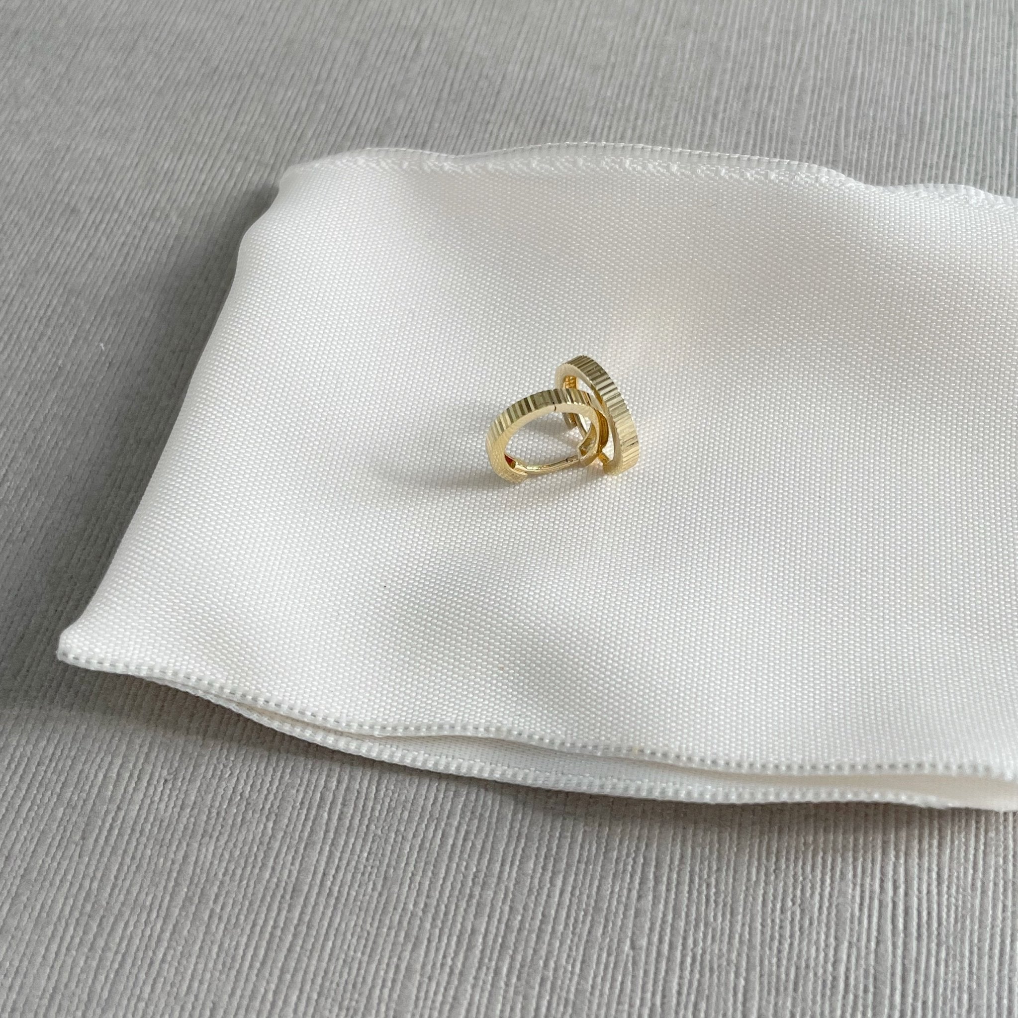 Solid Gold Ruth Huggies by Sarah Cornwell Jewelry. Solid gold tiny hoop huggie earrings on a white and gray background.