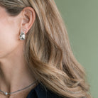 Close-up of a person wearing a chunky silver earring with a green background