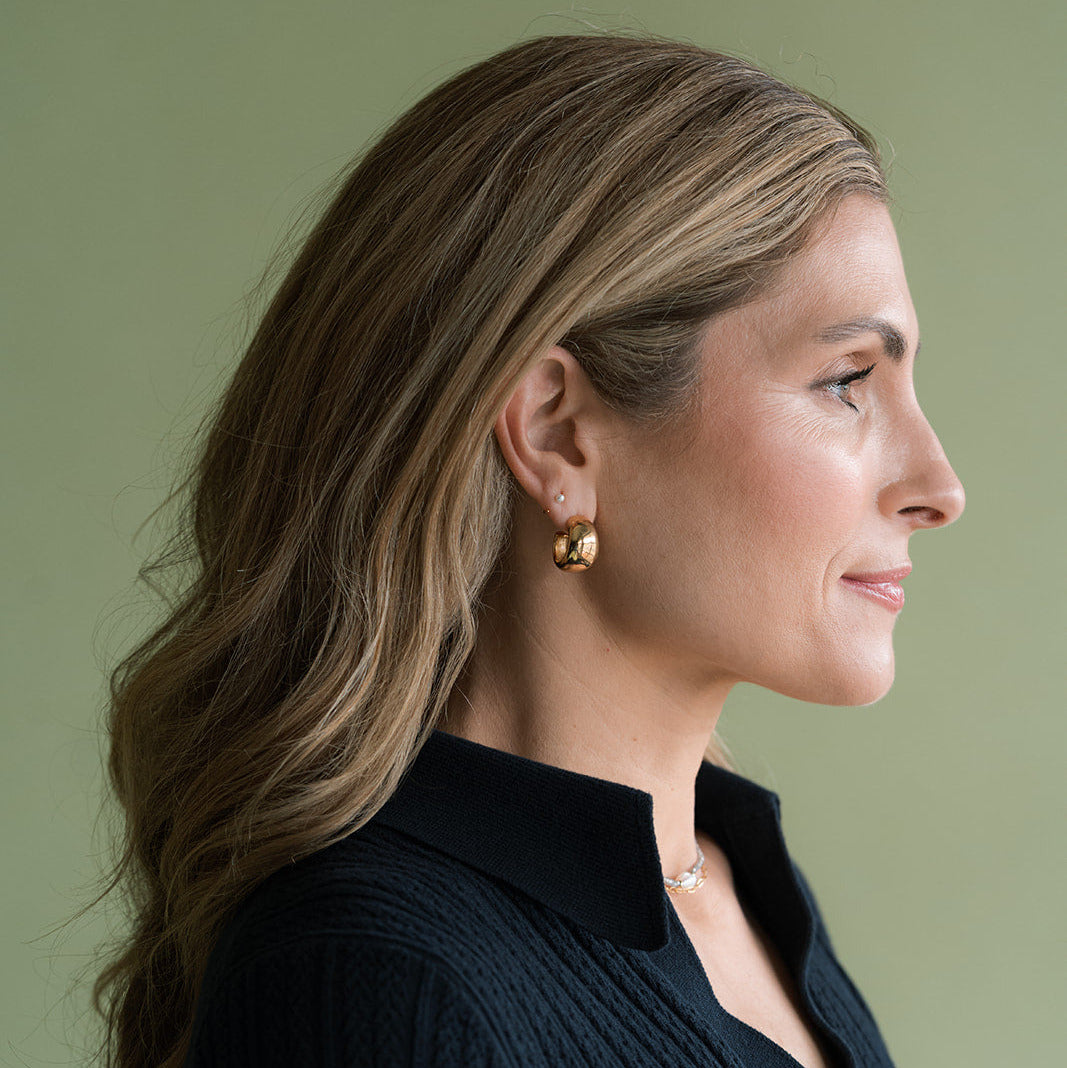 Profile view of woman wearing navy blue sweater and a chunky gold hoop