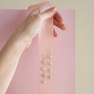 Hand holding pink ribbon with a pair of coin pearl statement earrings on a pink background