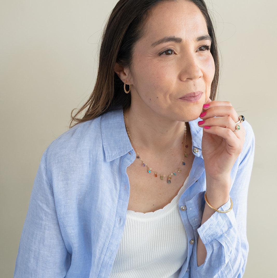 Woman wearing a light blue shirt over a white top, sitting against a plain background
