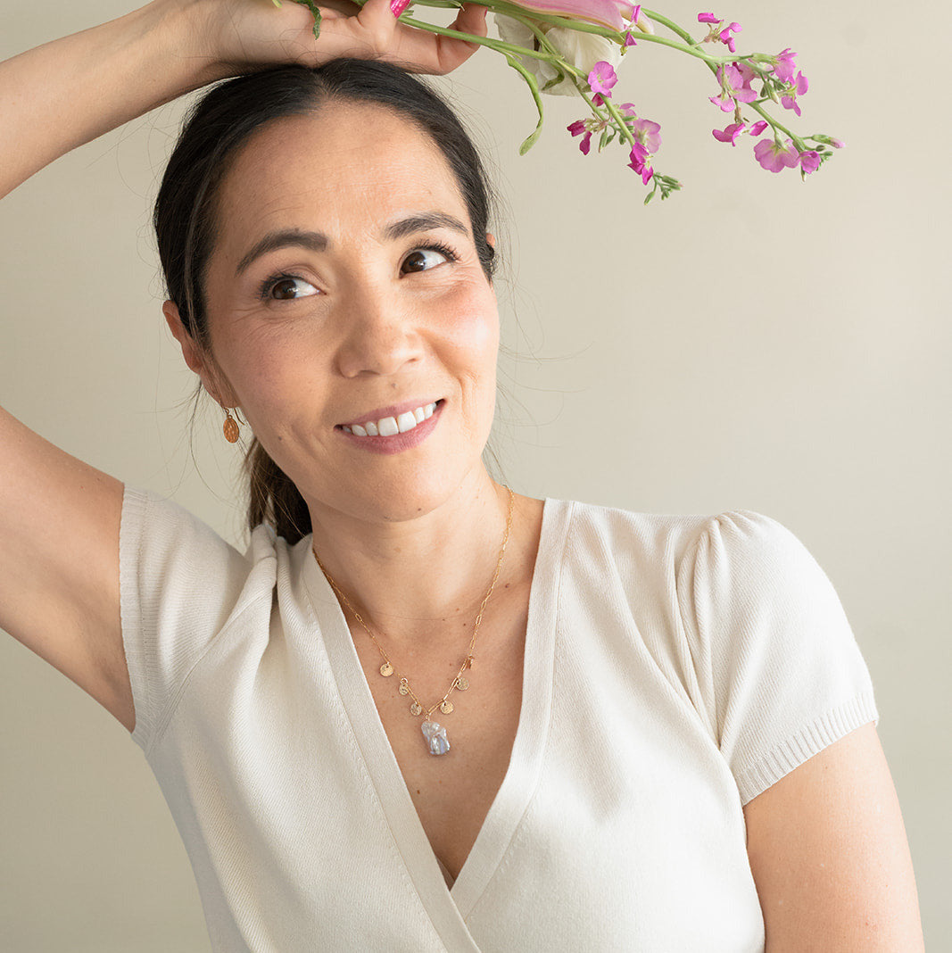 Smiling woman wearing a gold and baroque pearl necklace and holding flowers