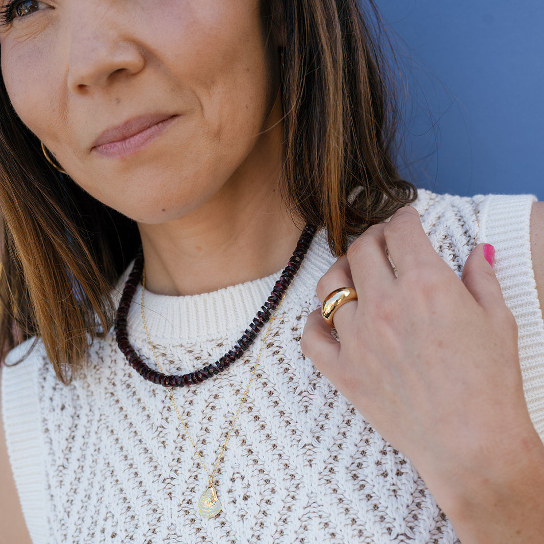 Woman wearing a white sleeveless top with jewelry including a necklace, ring, and bracelet.