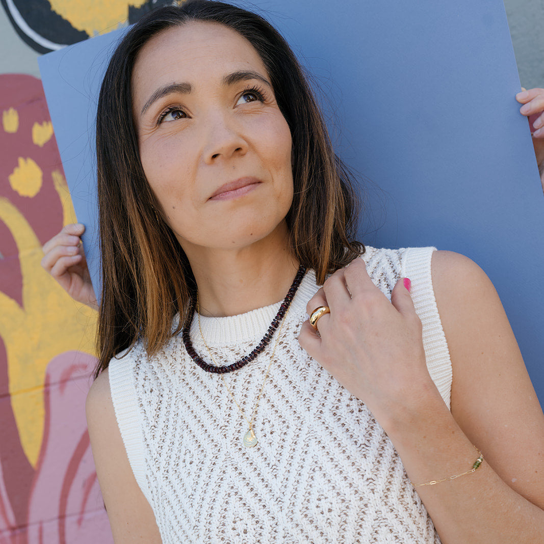 Woman wearing a white sleeveless crochet top against a colorful mural.