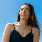 Woman wearing a navy dress and green agate necklace against a clear blue sky