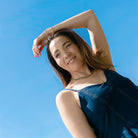 Woman in a blue dress wearing a green agate necklace against a clear blue sky