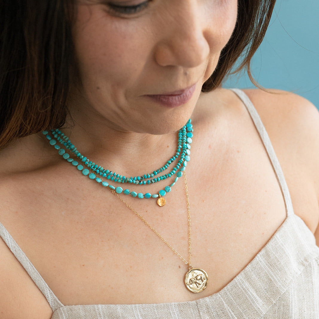Woman wearing two turquoise necklaces with a tan sundress