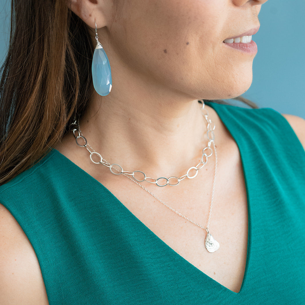 Woman wearing a green top with silver jewelry including a necklace and earrings.