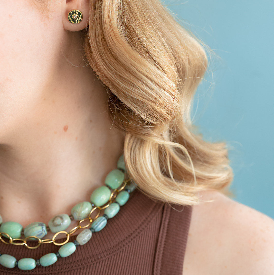 Close-up of a person wearing agate necklaces and gold earrings against a light blue background
