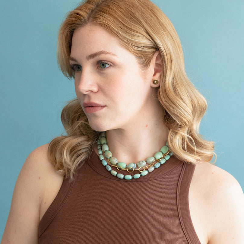 Woman wearing a brown sleeveless top and agate necklaces against a light blue background