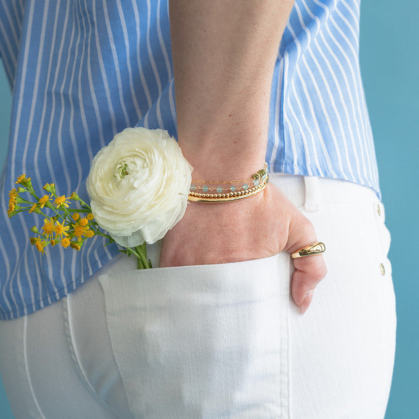 Person wearing a blue striped shirt and white pants with a white flower in their back pocket against a blue background