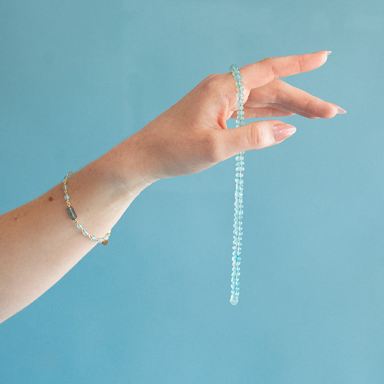 Hand holding an aqua chalcedony necklace and wearing a matching bracelet against a blue background