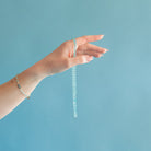Hand holding a knotted blue chalcedony necklace against a blue background