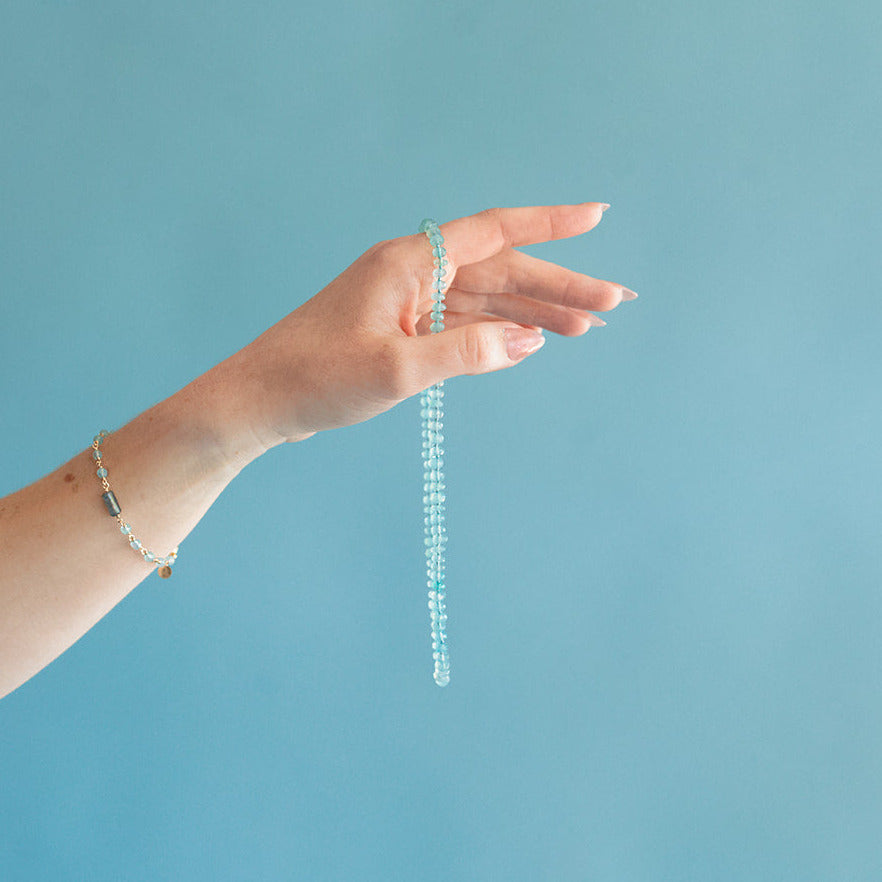 Hand holding a knotted blue chalcedony necklace against a blue background