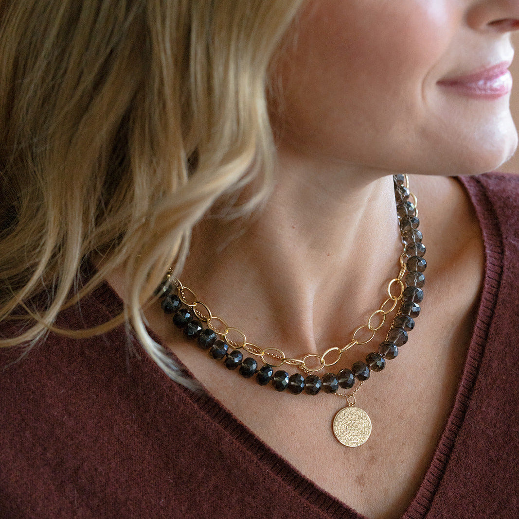 Close up of woman wearing smokey quartz gemstone necklace with layered gold necklaces