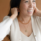 Woman smiling and putting on a gold pendant, layered with a topaz necklace