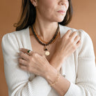 Woman in cream cardigan wearing layered gemstone and gold necklaces