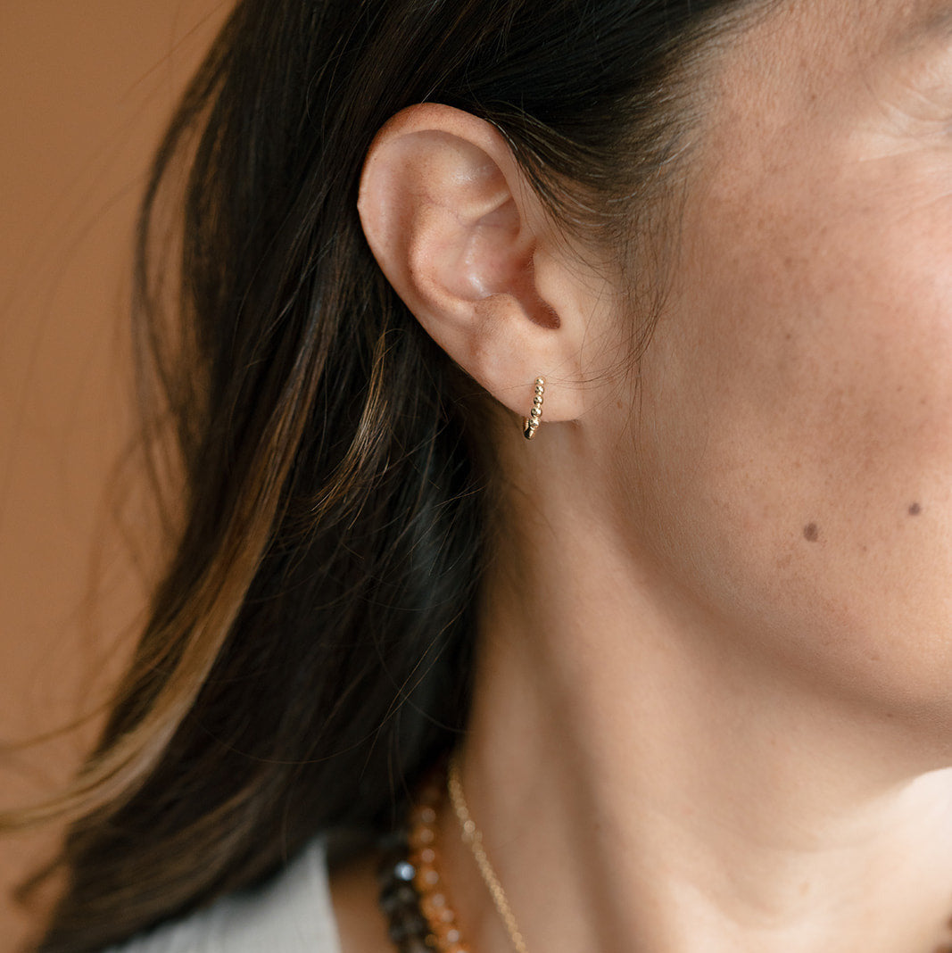 Close up of woman wearing a dainty solid gold huggie earring with beading detail