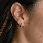 Close up of woman wearing a dainty solid gold huggie earring with beading detail