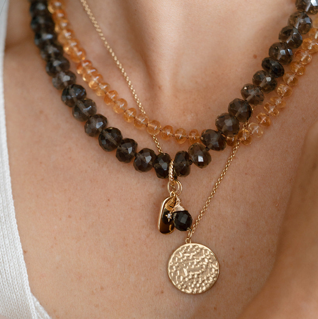 Close up of woman wearing stack of gemstone necklaces and a gold pendant