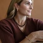Woman in a brown sweater with a gemstone necklace and layered gold jewelry