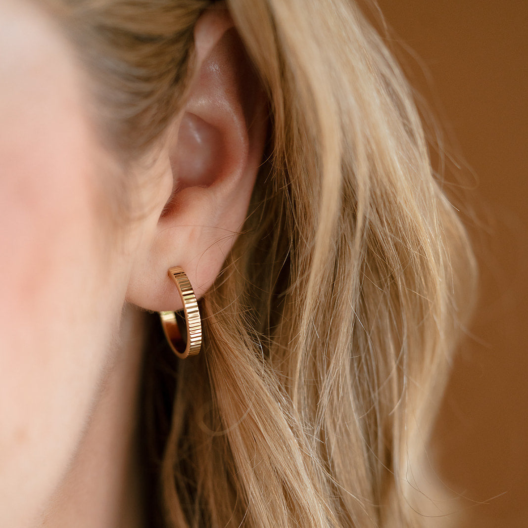 Close up of woman wearing hoop earring with ridged detail