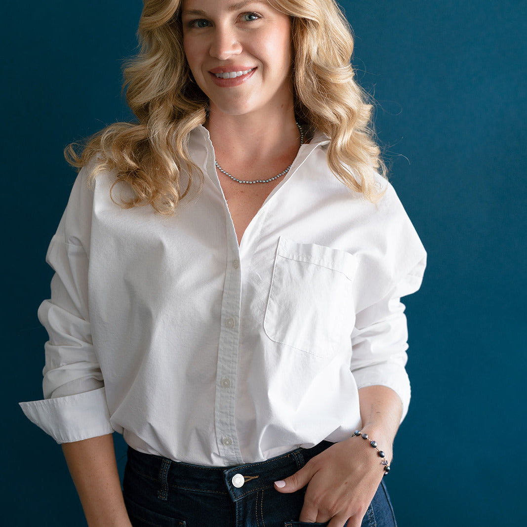 Woman wearing  small peacock pearl necklace and a white shirt