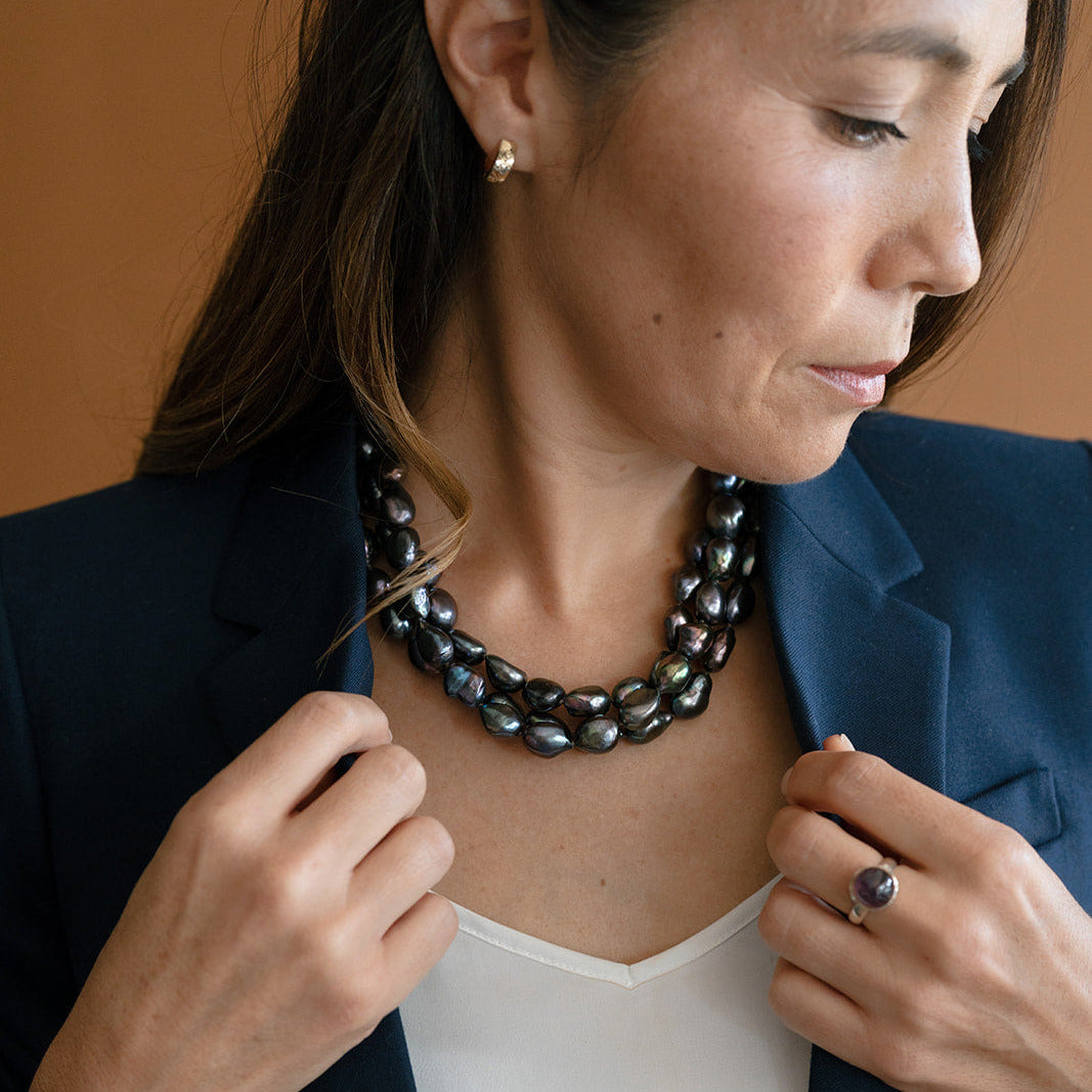 Woman wearing multiple peacock pearl necklaces and a navy blazer