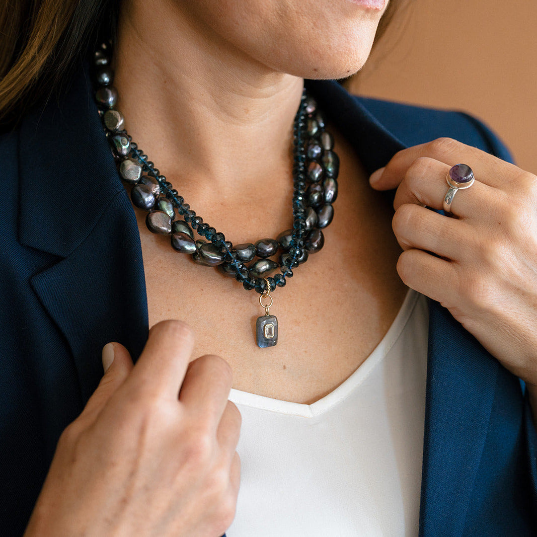 Woman wearing multiple peacock pearl necklaces and a navy blazer