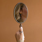 Woman holding mirror showing reflection of her wearing a peacock pearl earring