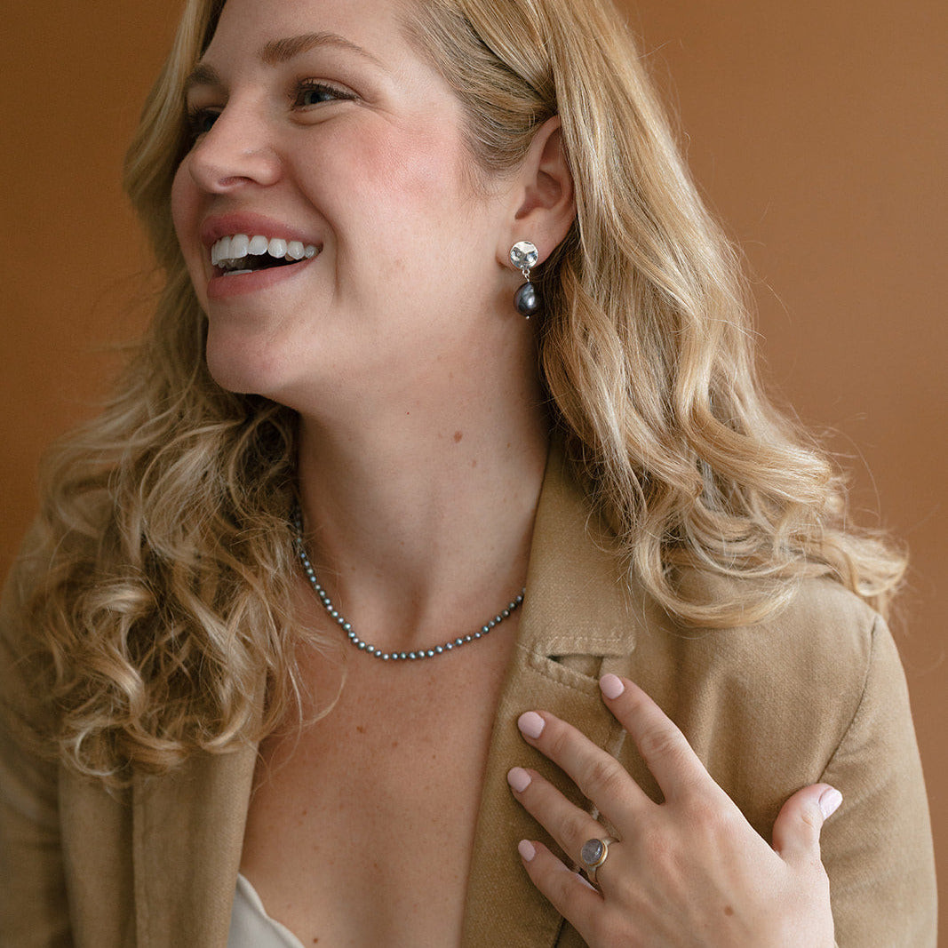 Woman wearing peacock pearl necklace and a camel colored blazer