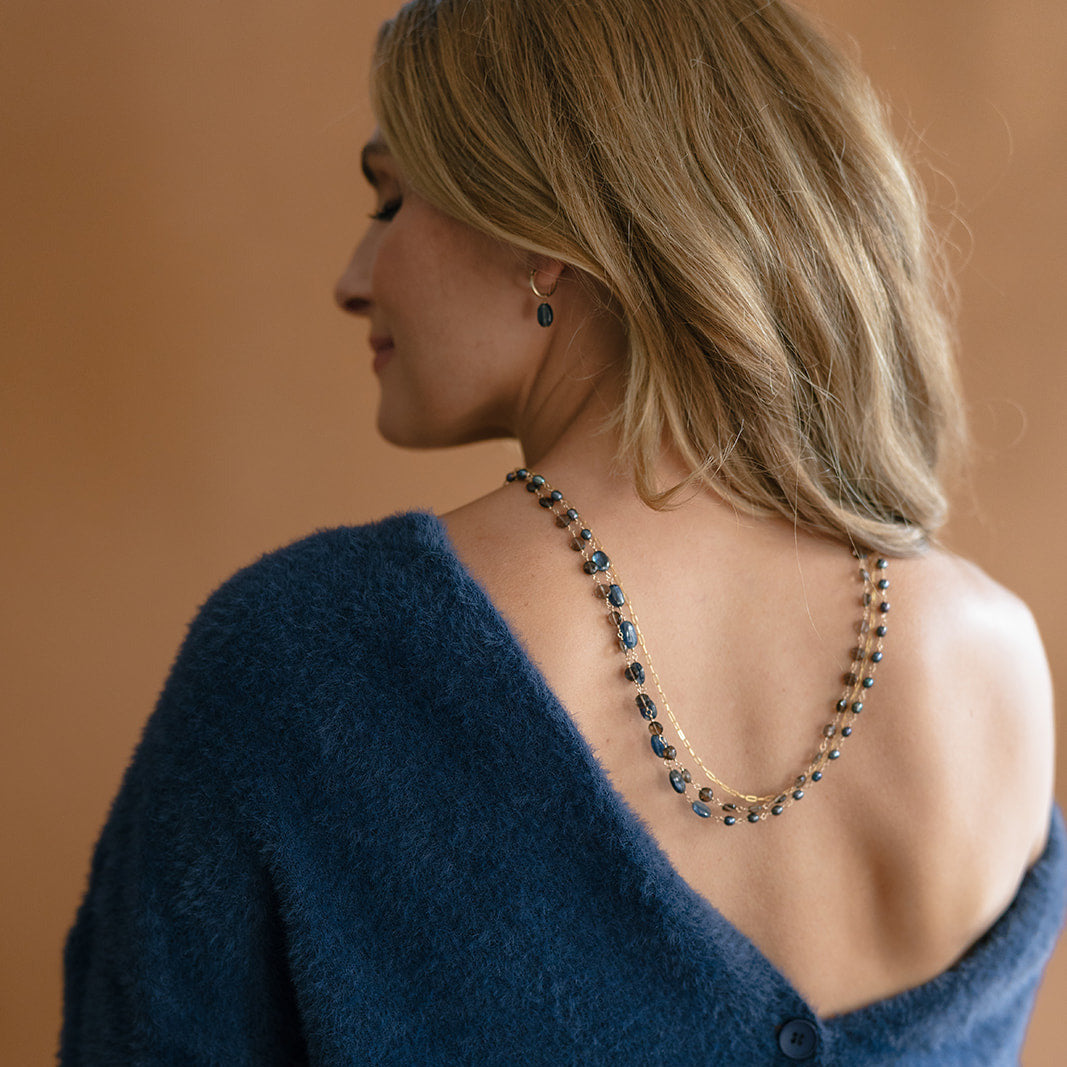 Woman wearing a triple strand necklace draped over her back and wearing a blue sweater