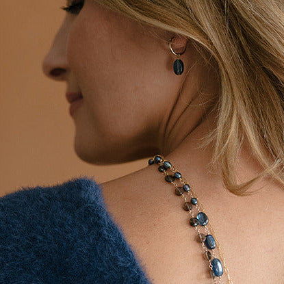 Woman wearing gold hoop earring with blue kyanite gemstone drop