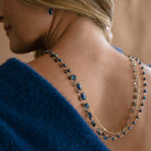 Woman wearing a triple strand necklace draped over her back and wearing a blue sweater