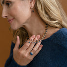 Woman holding a triple strand necklace draped over her back and wearing a blue sweater