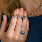 Woman holding a triple strand necklace draped over her back and wearing a blue sweater