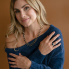 Woman wearing a triple strand necklace draped over her back and wearing a blue sweater