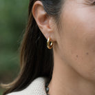 Close-up of a person wearing gold hoop earrings with a blurred green background