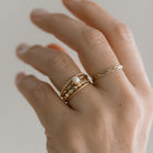 Hand wearing a gold ring stack on a neutral background