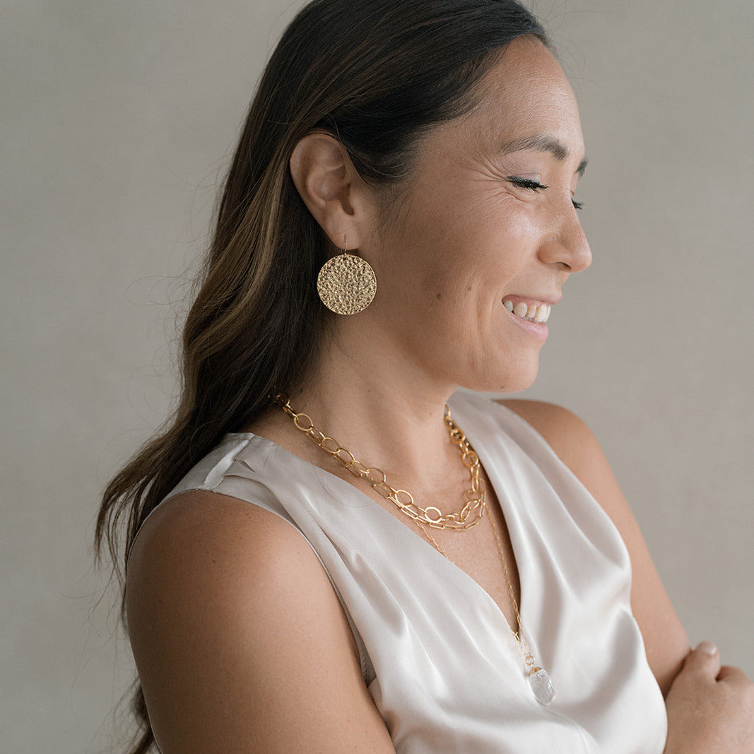 Woman wearing layered gold necklaces with a silk top and gold statement earrings
