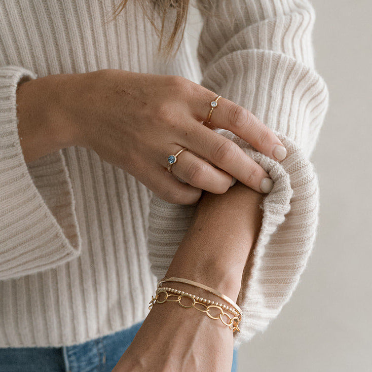 Person wearing a beige sweater and blue jeans with gold jewelry on a plain background