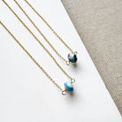 Two necklaces with a single small Golden Hill turquoise bead on gold chains on a white surface.