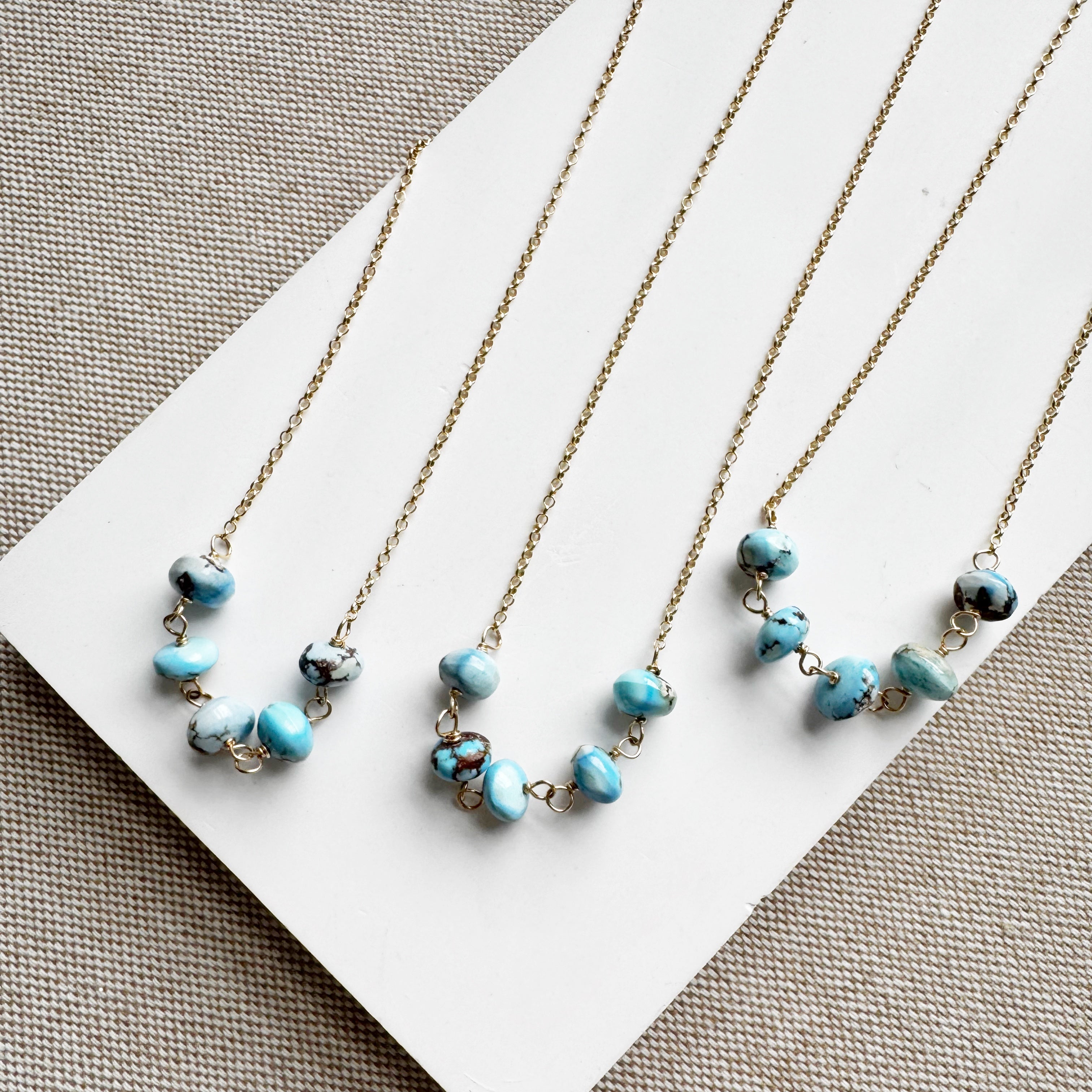 Three gold necklaces with Golden Hills turquoise beads on a white card against a beige background