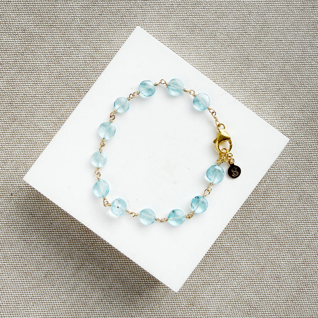 Blue quartz bracelet on a white card with a gold clasp on a beige surface