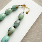 Clasp detail of necklace with teal agate beads on a white card