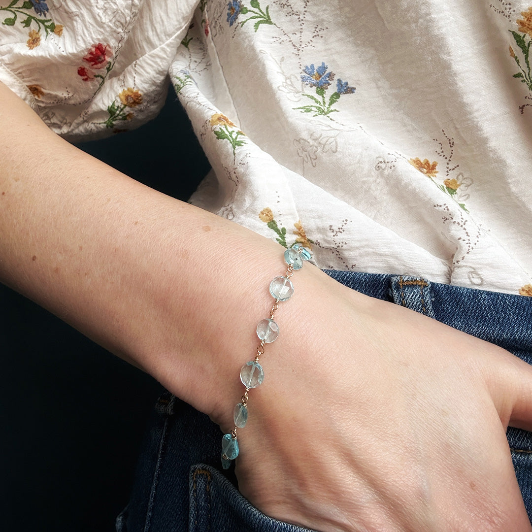 Close-up of a wrist wearing a blue quartz bracelet with a floral-patterned garment in the background